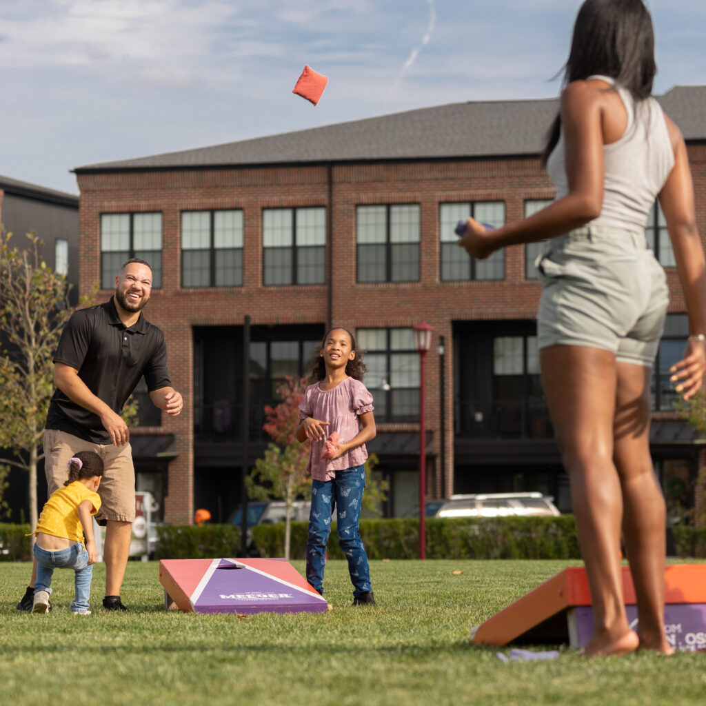 Family playing cornhole on Meeder Green in Meeder neighborhood built by Charter Homes and neighborhoods.